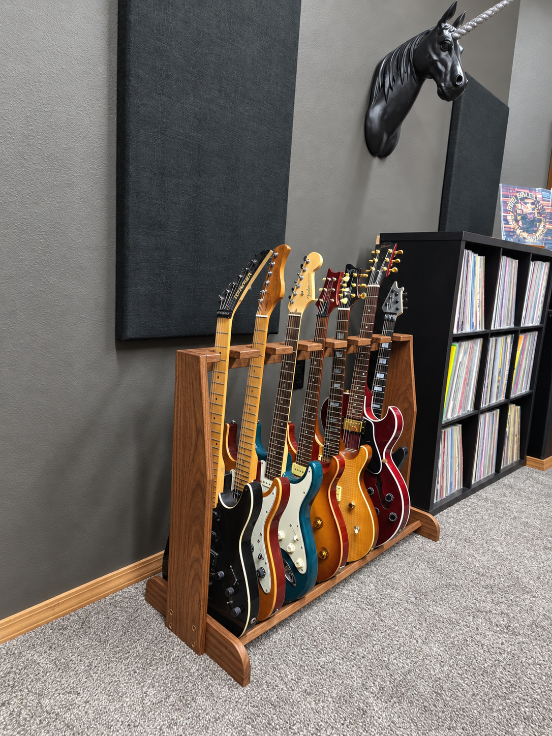A wooden floor-standing rack holding several electric guitars against a grey wall beside a shelf of records.